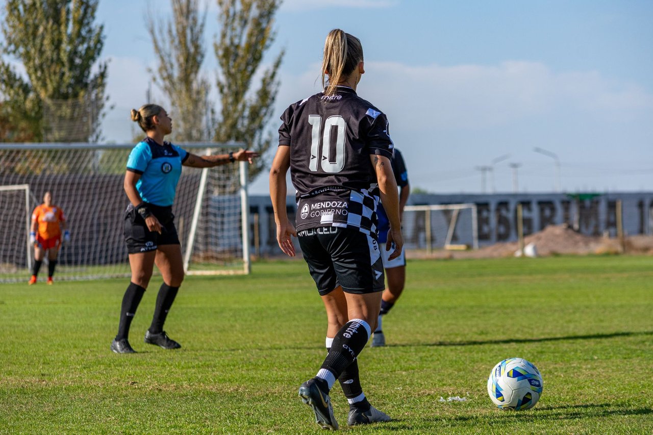 Jogadoras disputam uma partida de futebol feminino ao ar livre em um estádio.