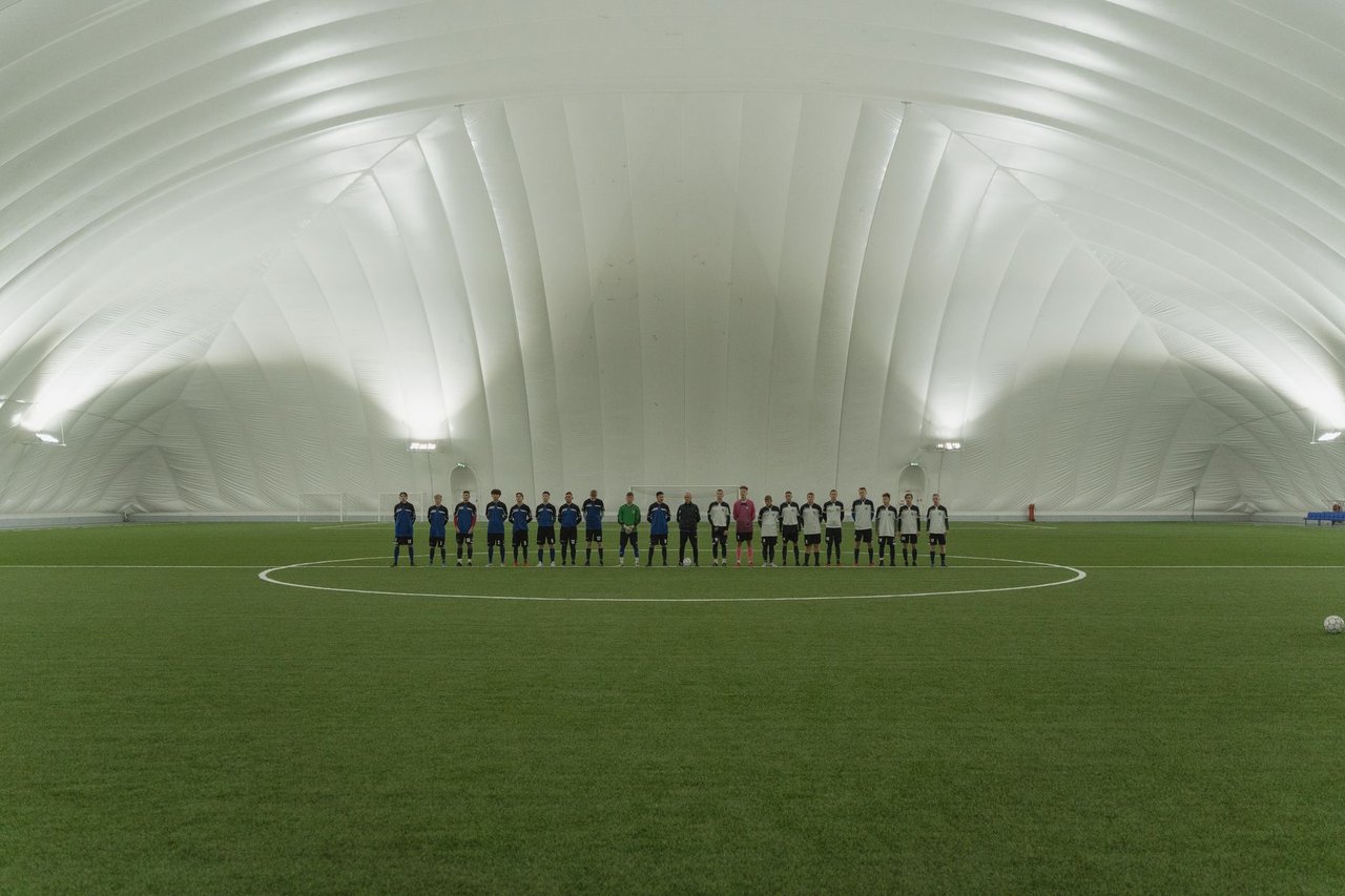 Duas equipes juvenis de futebol alinhadas em um campo de grama sintética sob a iluminação de um estádio coberto.