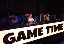 Jogadores de e-sports competem em equipe durante um torneio, diante de computadores e telas.
