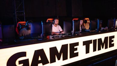 Jogadores de e-sports competem em equipe durante um torneio, diante de computadores e telas.