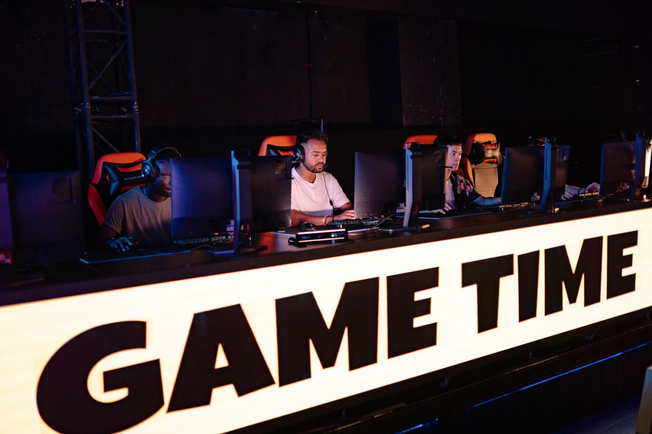 Jogadores de e-sports competem em equipe durante um torneio, diante de computadores e telas.