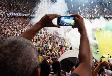 Torcedores registram com um smartphone a atmosfera de uma partida de futebol nas arquibancadas.
