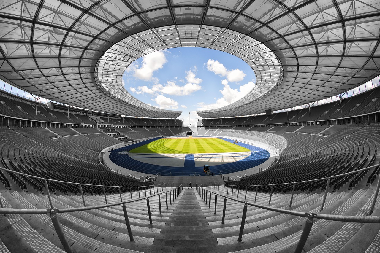 Vista ampla e simétrica de um estádio de futebol vazio, com o campo ao centro.
