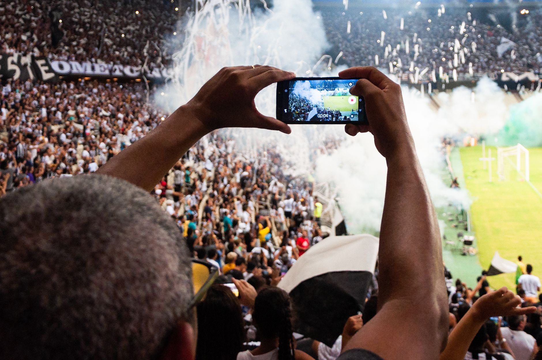 Torcedores registram com um smartphone a atmosfera de uma partida de futebol nas arquibancadas.
